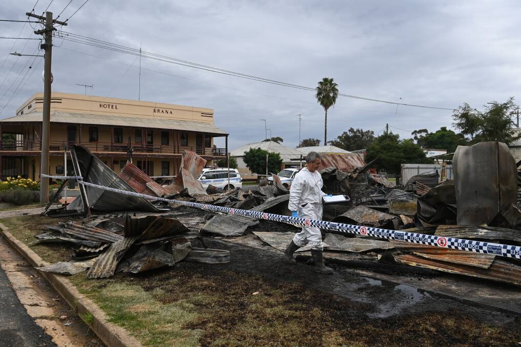 INVESTIGATION: A fire investigator searches through the flattened Urana business on Monday. Nearby resident Julie Barker thought the fire started in an area with chemicals and garden supplies. Pictures: MARK JESSER