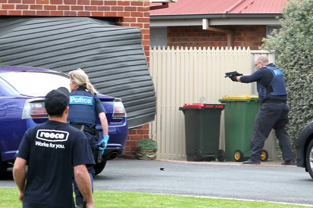 ARMED: A police officer aims at the man's stolen vehicle as he rams it through a closed roller door. 