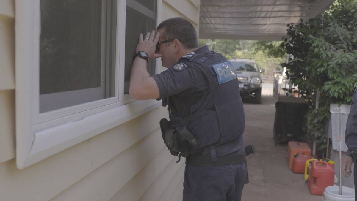 DOOR KNOCK: A police officer inspects a home in Whitfield. Tens-of-thousands of hectares are burning in the area. 