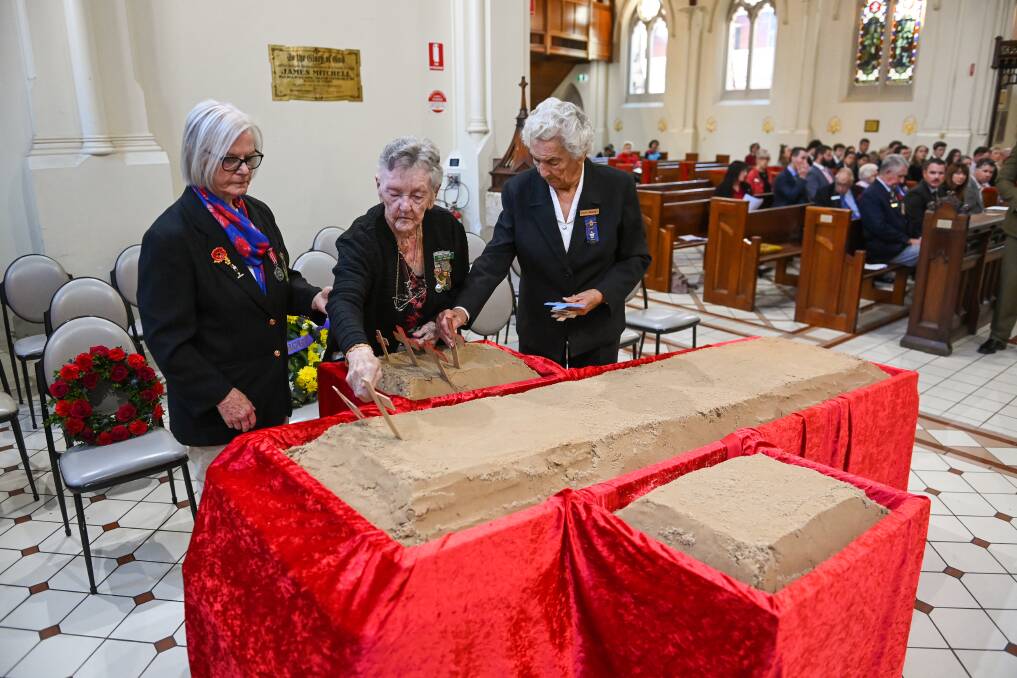Marj Howard watches as Pat Freyer and Sylvia Bradney, of Albury and District War Widows, place crosses in the bed of sand. Picture by Mark Jesser