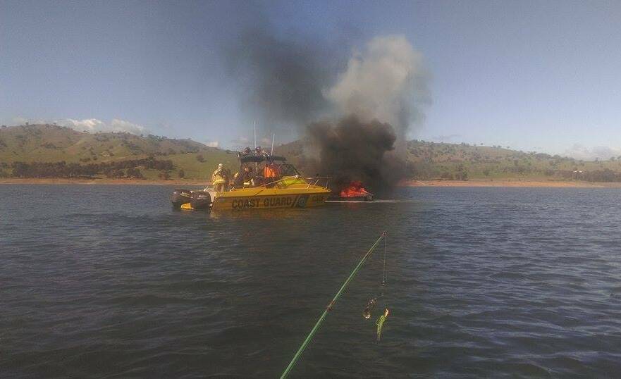 FIGHTING THE FIRE: Emergency workers on the Lake Hume Coast Guard boat attack the blaze before towing the damaged boat to shore. Picture: DOUG HITCHENS