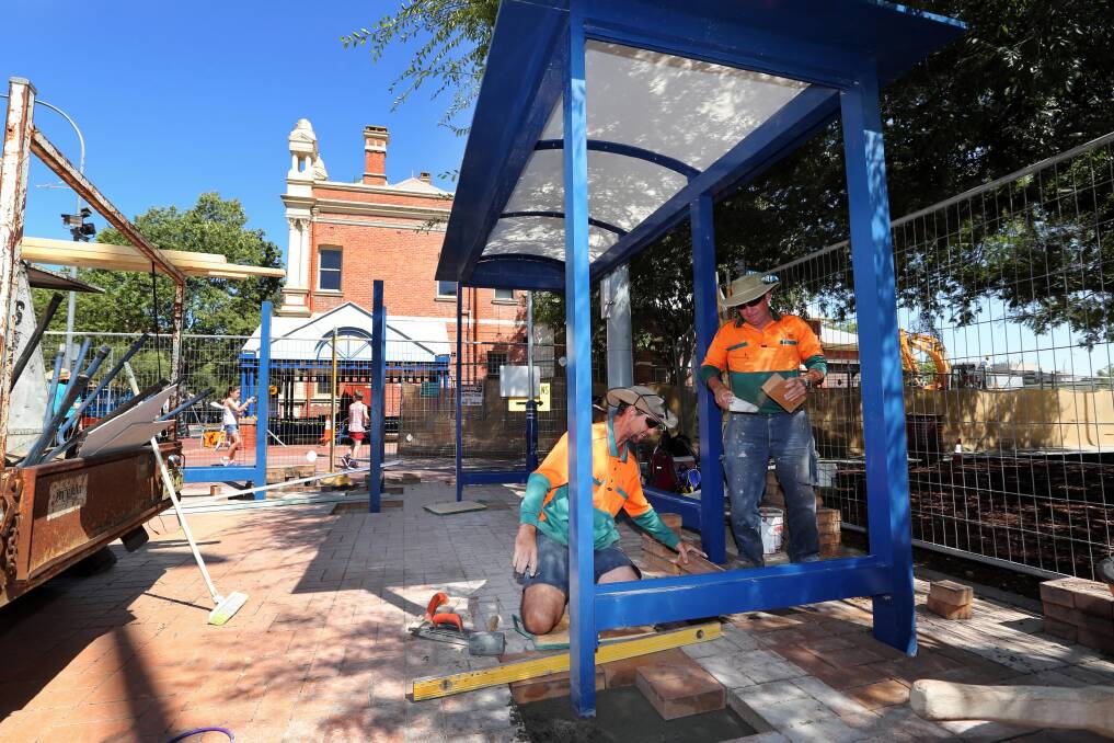 Scott Lynch and Roy Fulford, from Albury City’s engineering department, construct a new bus shelter at QEII Square, Dean Street, Albury, while the existing one is demolished. Picture: MATTHEW SMITHWICK