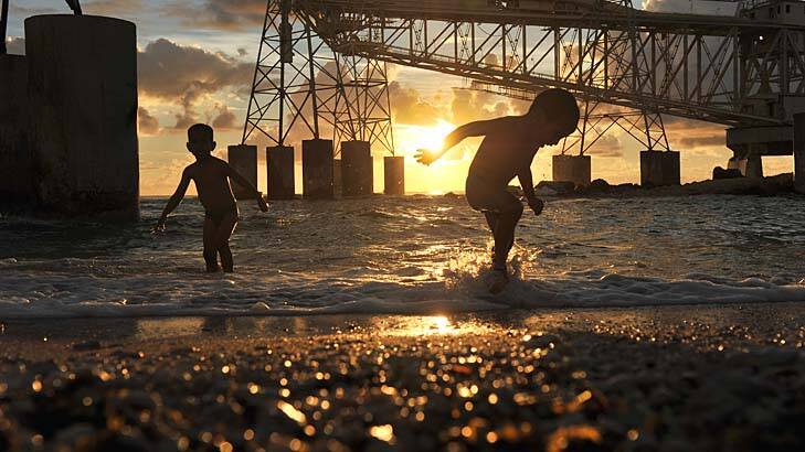 Nauruan children play at the the water's edge beneath cranes used to load and unload container ships at the remote Pacific island, now reinstated as an assylum seeker holding camp.
