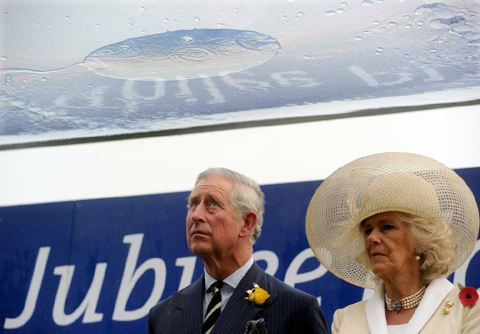 Prince Charles stands with Camilla waiting to present the trophy under cover from the pouring rain after the Diamond Jubilee won by Eclair Suprise at Flemington.