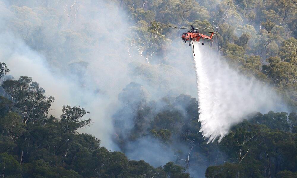 A water-bombing helicopter tackles the fire in near-inaccessible country yesterday. Pictures: JOHN RUSSELL