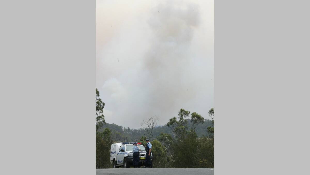 With a smoke plume rising in the distance, police officers direct traffic away from the rural roads in Brogo under threat from an out of control bushfire on Tuesday.