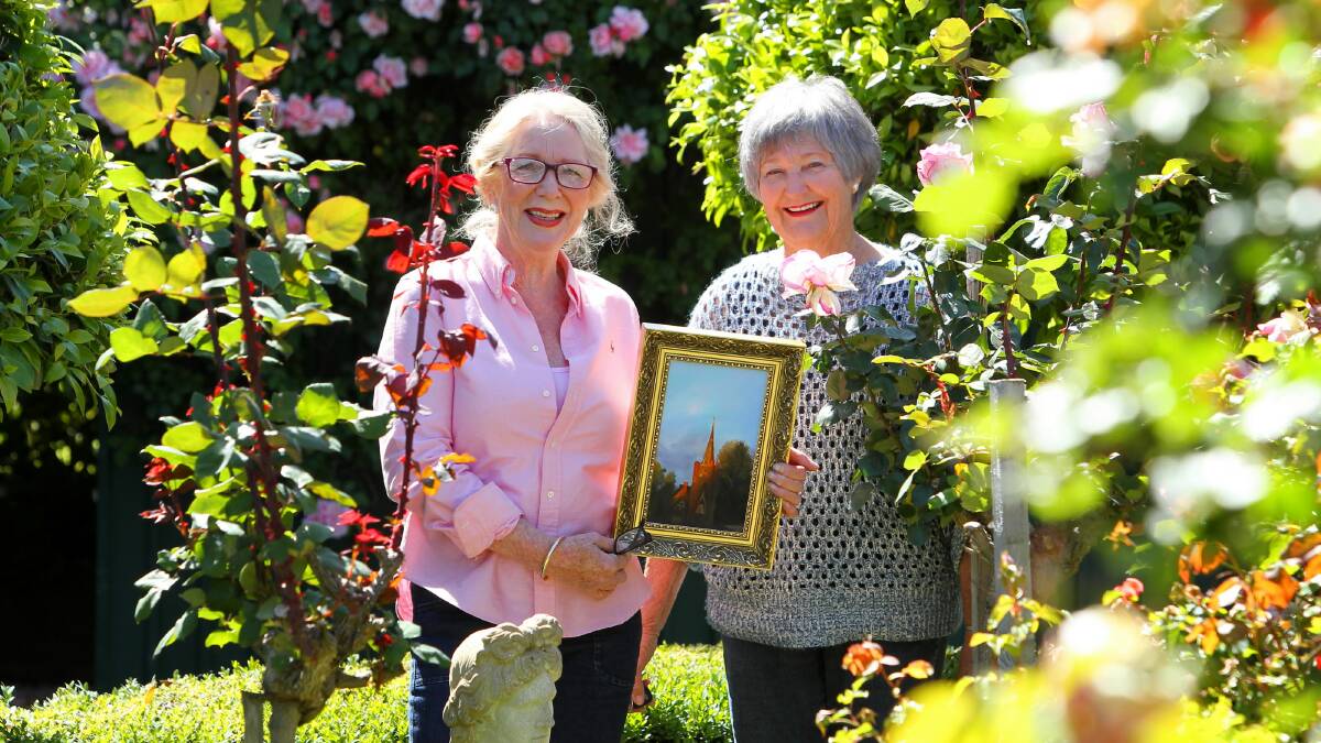 Artist Marilyn Byrnes in her rose garden holding her painting of St David’s Uniting Church, with Rose-a-Fair organiser Beryl Gorring. Picture: MATTHEW SMITHWICK