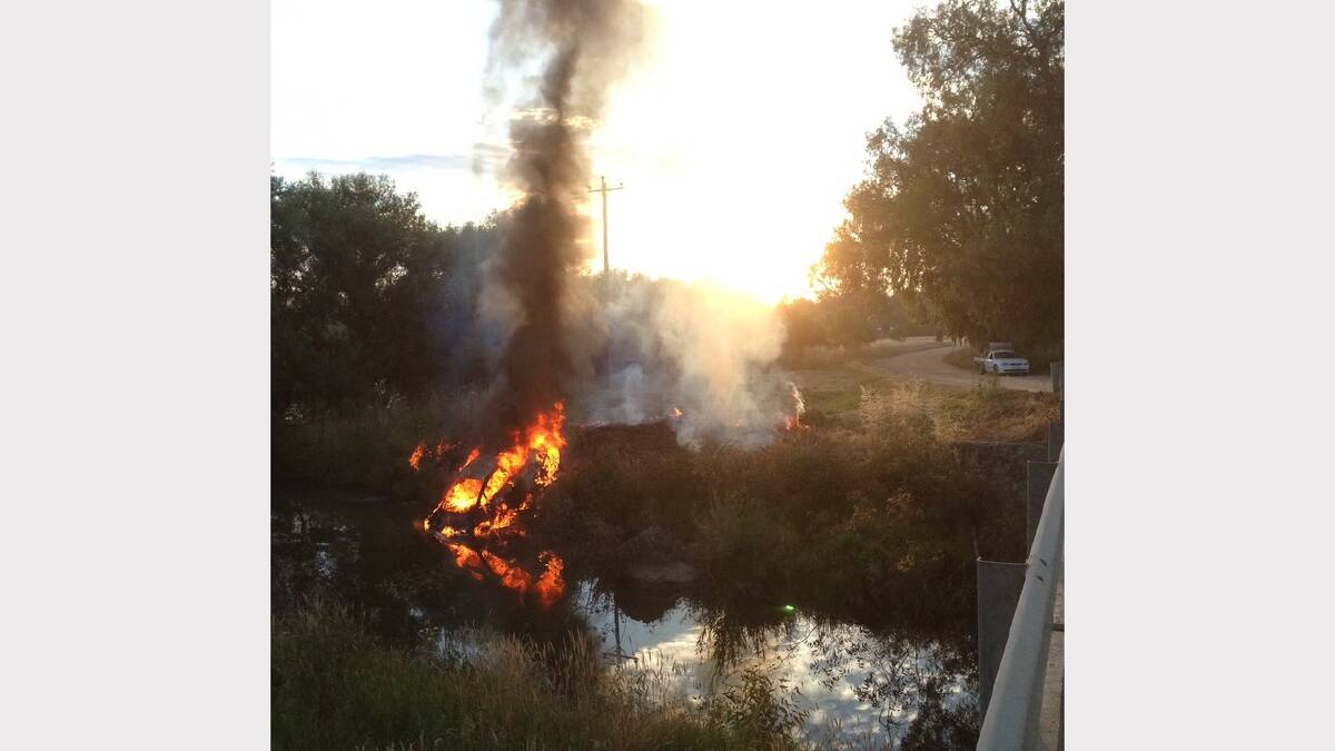 Flames erupt from a car after it was dumped on banks of a tributary of the river. Picture: DAVID HAWKINS